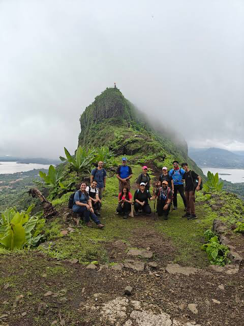 Group of trekkers standing together on a lush green Sahyadri mountain ridge overlooking the misty valley