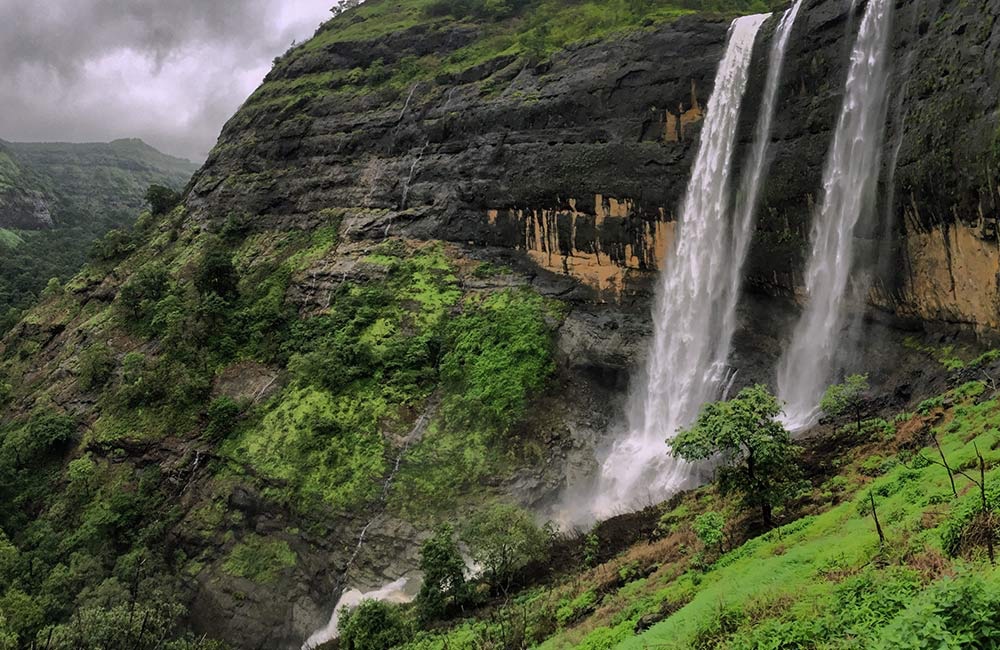 Twin waterfalls cascading down lush green Sahyadri mountain cliff faces in monsoon